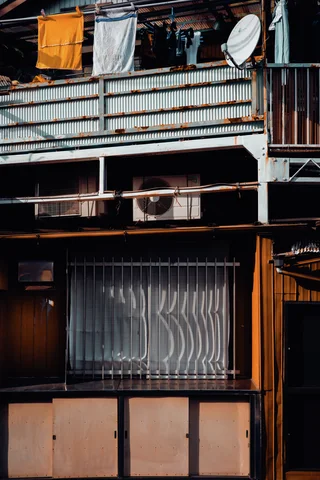 Laundry hangs above a corrugated balcony railing over a barred lower window and wood-paneled facade.