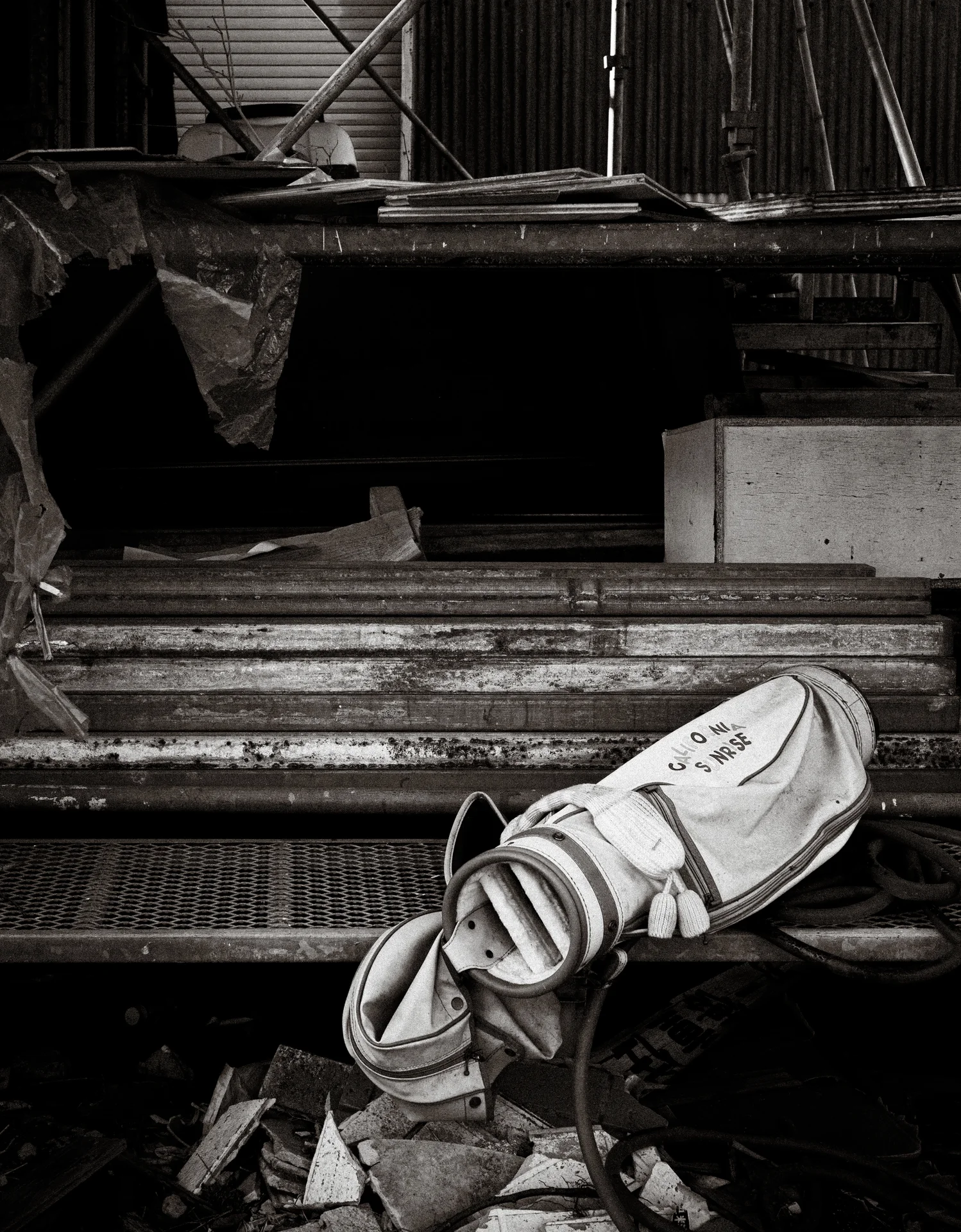 A pair of worn light shoes rests among scrap metal and pipes in black and white.