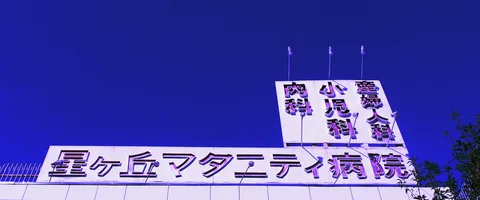 Large Japanese rooftop lettering rises above a pale building against a deep blue sky.