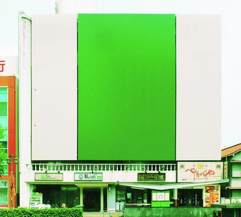 A large blank green panel dominates a white commercial facade above small signs and ground-floor entrances.