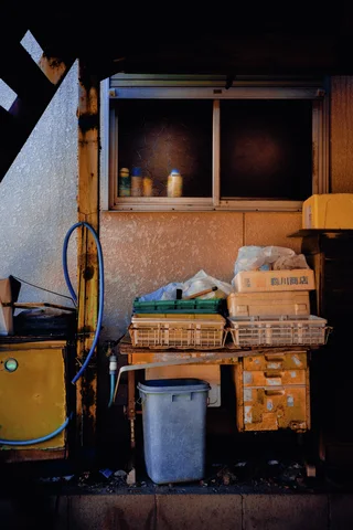 Baskets, boxes, and a pale bucket cluster beneath a small window beside a coiled hose.