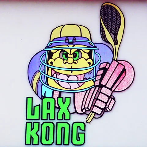 A cartoon gorilla wearing a helmet grips a lacrosse stick above green LAX KONG lettering.