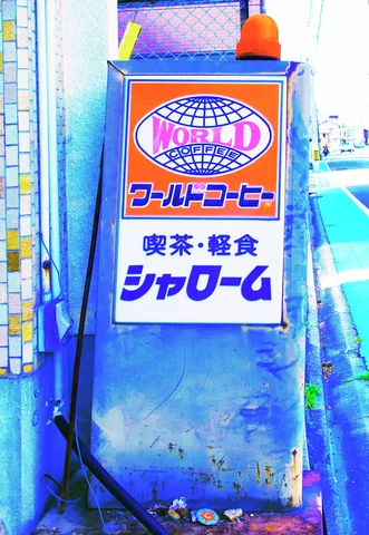 An orange and blue World Coffee sign stands on a blue pedestal beside a narrow sidewalk.
