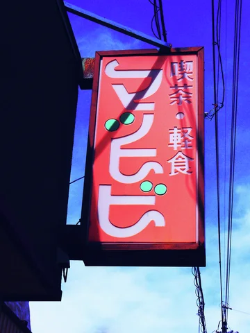 A tall red cafe sign projects beneath overhead wires against a vivid blue sky.
