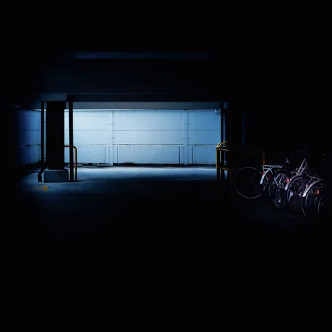 A pale blue illuminated opening glows at the end of a dark passage beside parked bicycles.