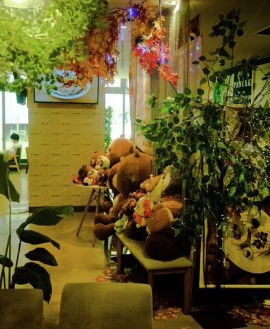 Potted greenery and plush animals crowd a warmly lit shop interior near a bright doorway.