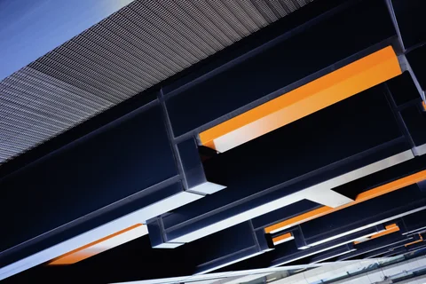Dark angular beams with bright orange strips form a geometric pattern beneath a corrugated roof.
