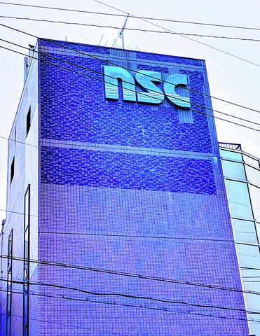 Large turquoise lettering marks the upper corner of a tall blue-tiled building crossed by utility wires.