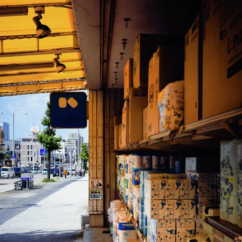 A yellow translucent canopy shelters stacked printed boxes beside a sunlit sidewalk.