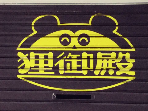 A yellow cartoon animal face encloses bold Japanese characters on a dark ribbed shop shutter.