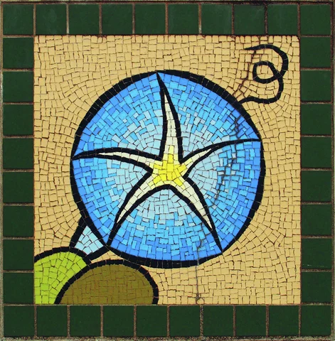 A round blue flower with a pale star-shaped center forms a mosaic bordered by dark green tiles.