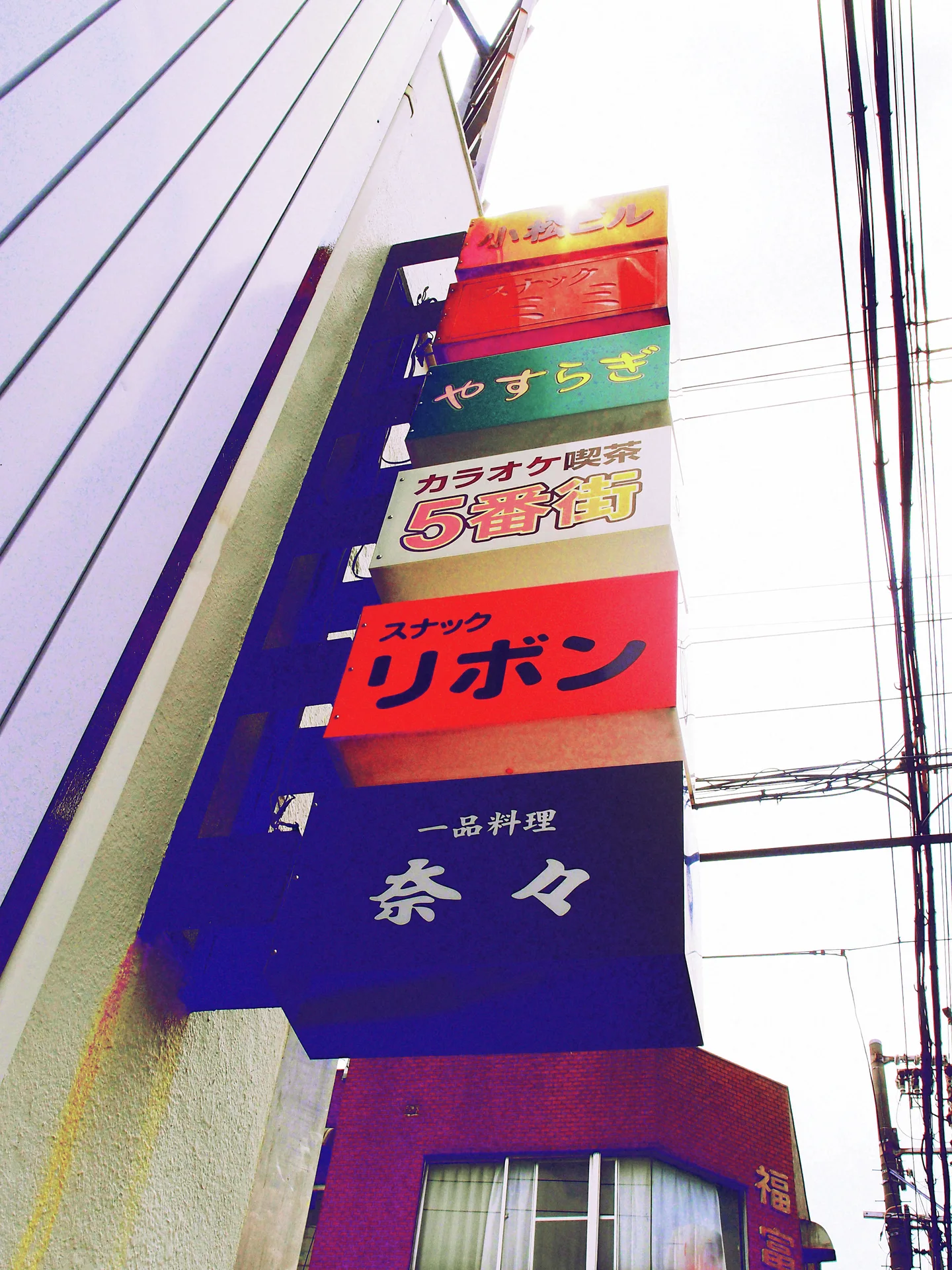 A tall stack of colorful business signs projects from a building beside overhead wires.