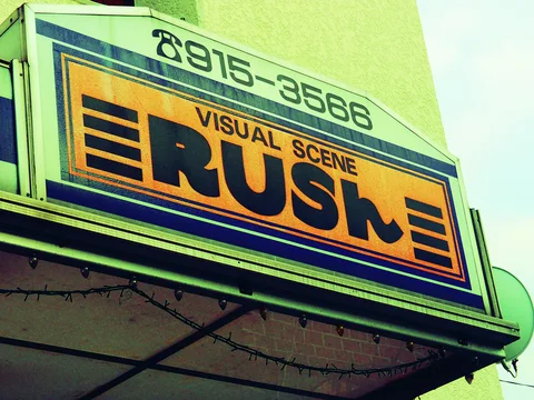 Bold black RUSH lettering fills an orange-and-blue projecting sign beneath a curved green telephone panel.