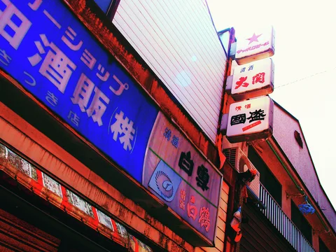 Blue and pale shop signs angle above a weathered storefront beside stacked projecting signs.