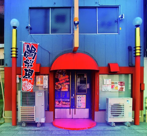 A red semicircular canopy crowns a purple entrance between two air conditioners on a blue facade.