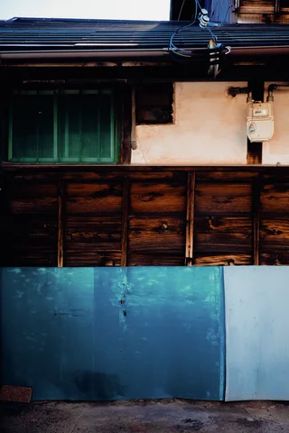 Turquoise metal panels line the base of a weathered wooden house beneath a dark window.
