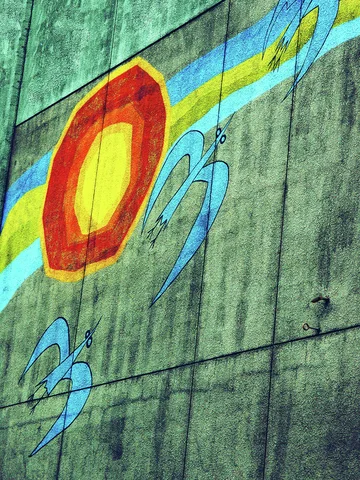 Blue bird shapes and a red and yellow sun decorate a weathered concrete wall crossed by utility wires.
