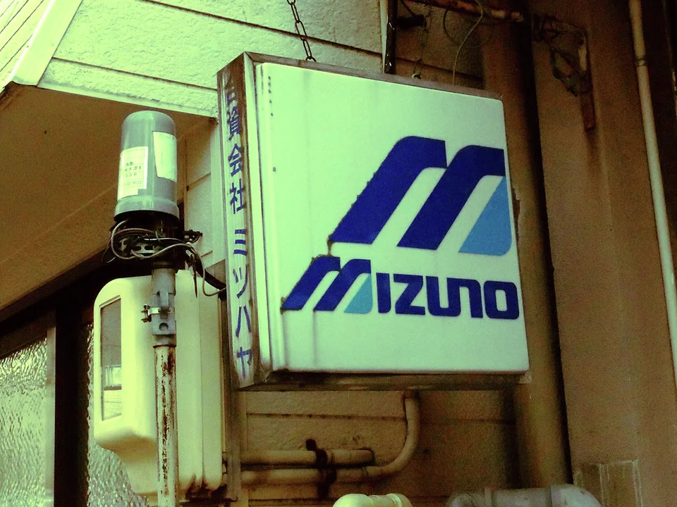 A pale Mizuno logo sign projects from a beige wall beside a narrow cylindrical fixture.