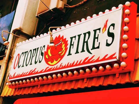 A bulb-lined restaurant sign displays an illustrated red octopus above a band of painted flames.