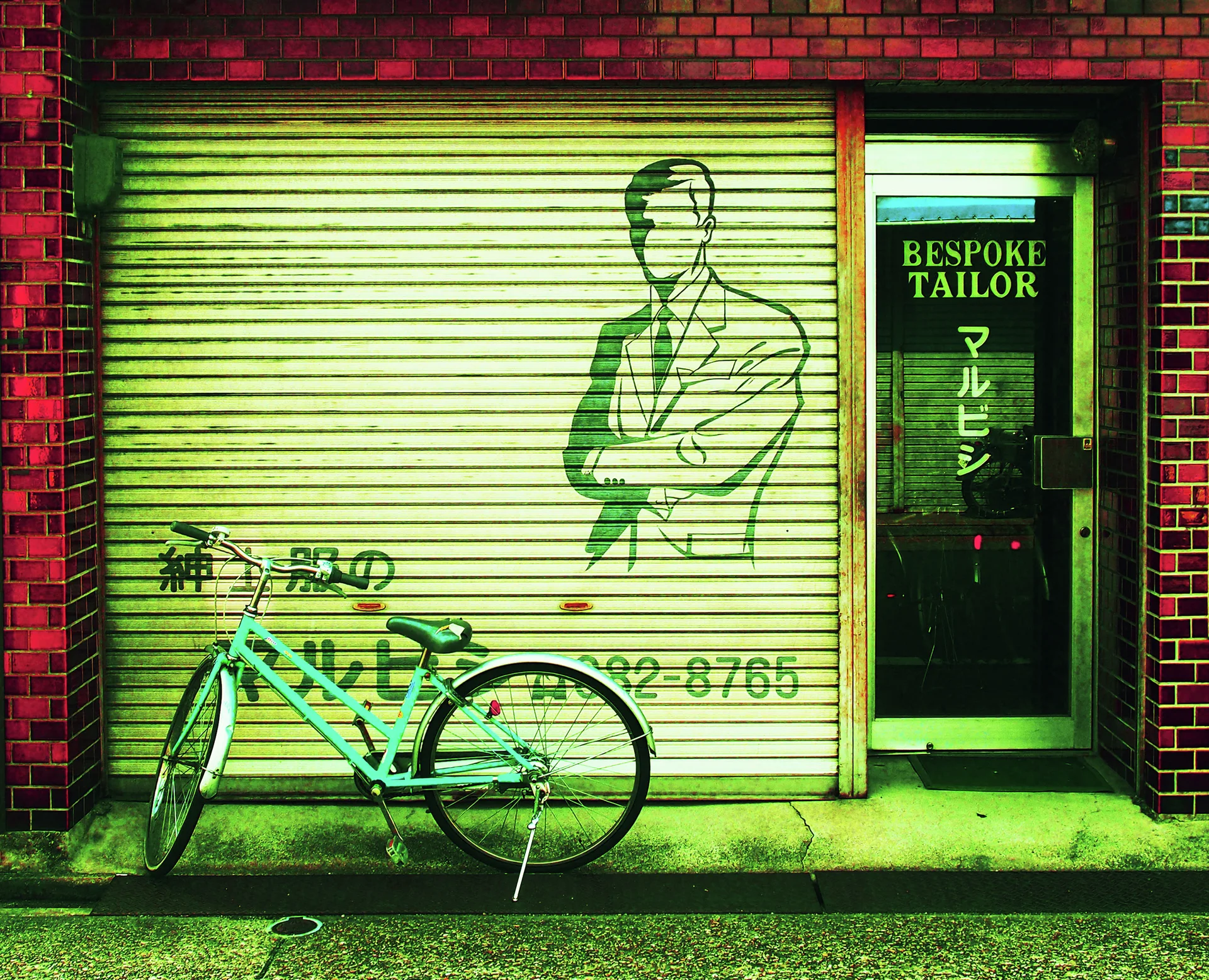 A green bicycle leans before a tailor's shutter illustrated with a suited man.