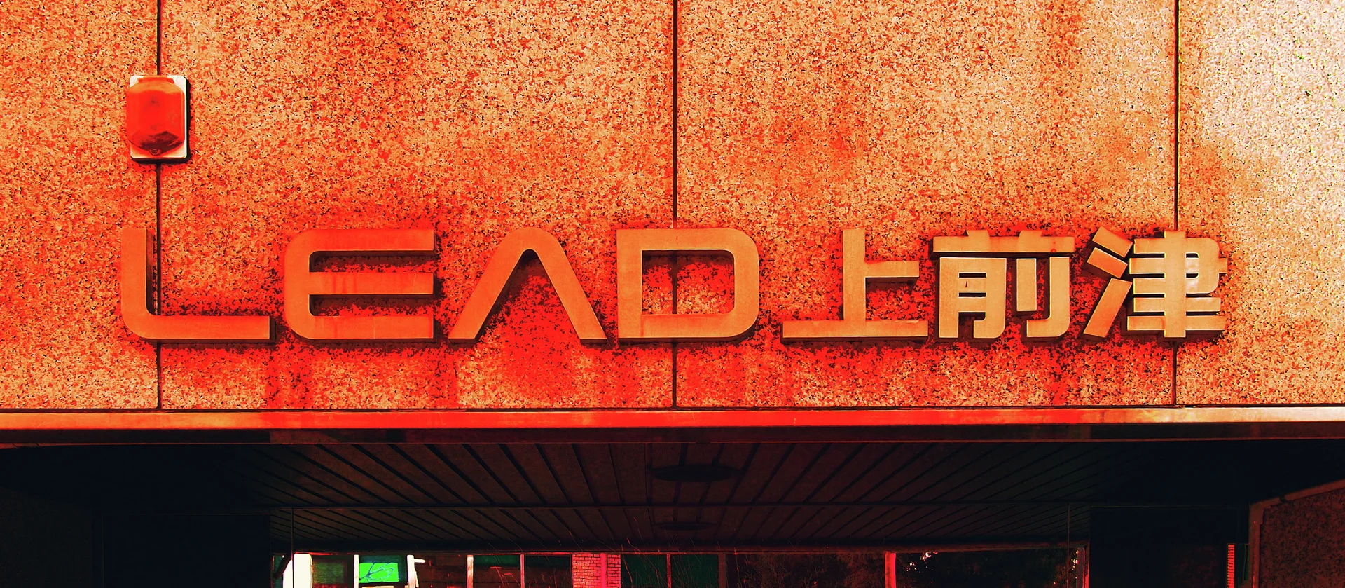 Red raised lettering and pale Japanese characters stretch across an orange textured facade above a dark overhang.