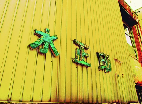 Three weathered green characters are mounted on a bright yellow corrugated wall.
