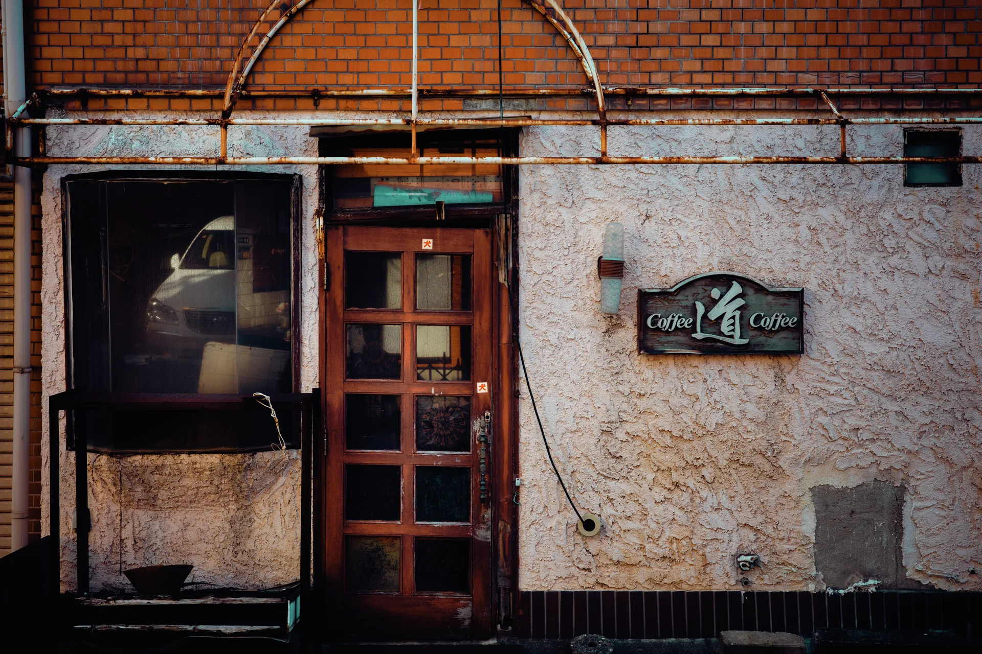 A narrow wood-framed door and dark cafe sign interrupt a cracked wall beneath exposed pipes.