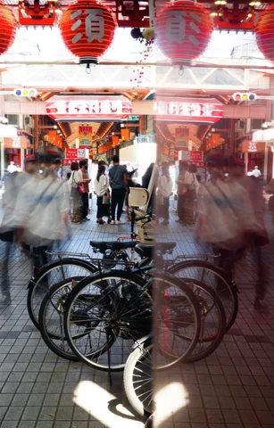 Bicycles and blurred reflections fill the foreground beneath red lanterns at a busy covered passage.