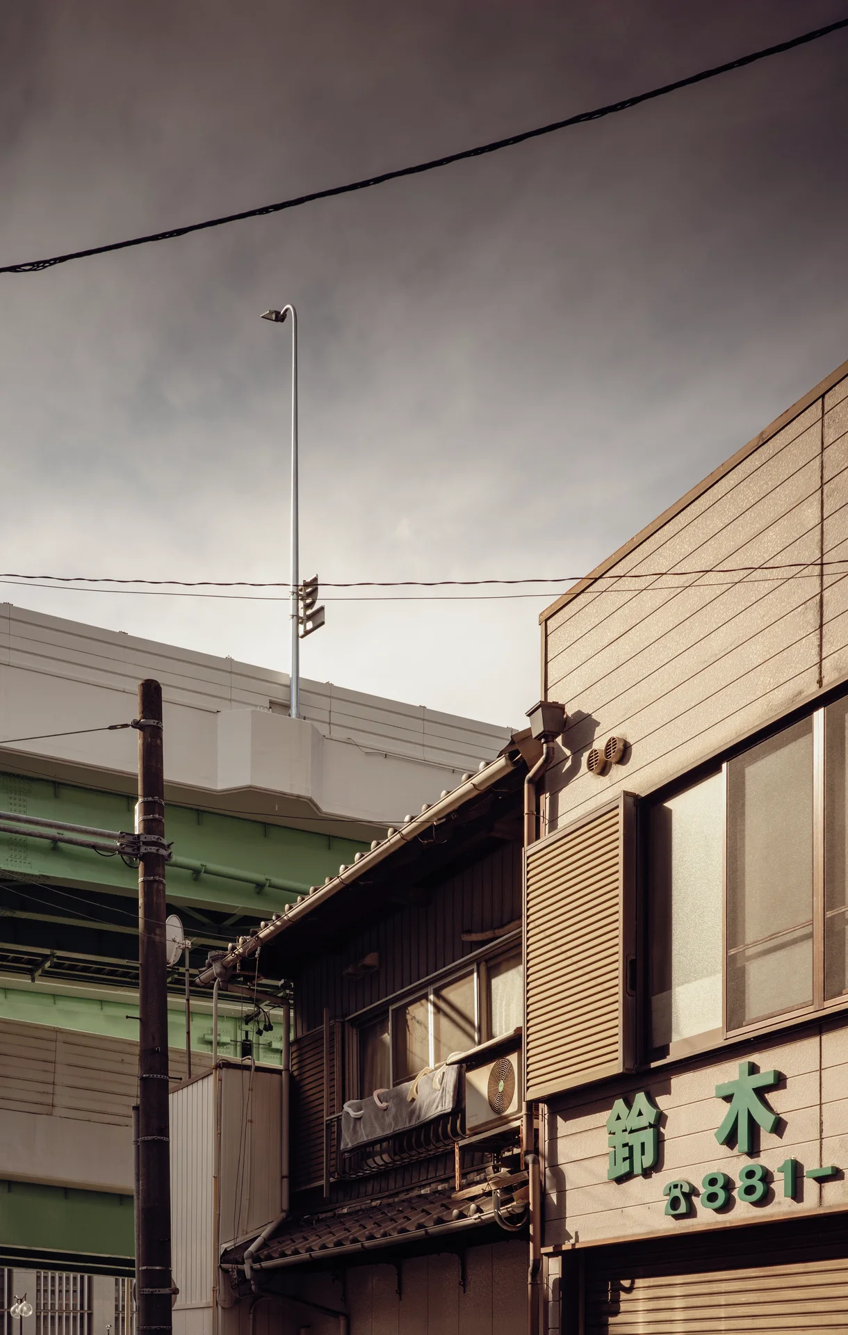 Low storefront roofs and upper windows rise beneath crossing utility wires and a tall antenna against gray clouds.