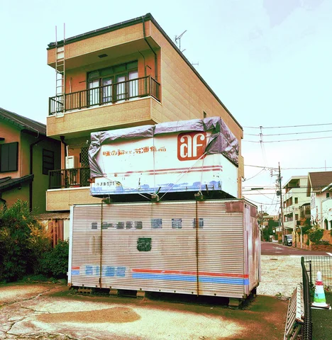 A closed metal kiosk stands before a pale orange building with balcony railings.