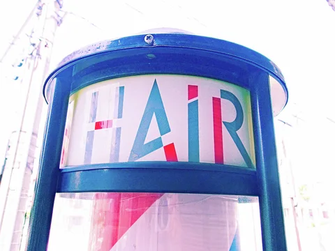 A blue-framed cylindrical barber sign displays colorful Hair lettering above diagonal red and white stripes.