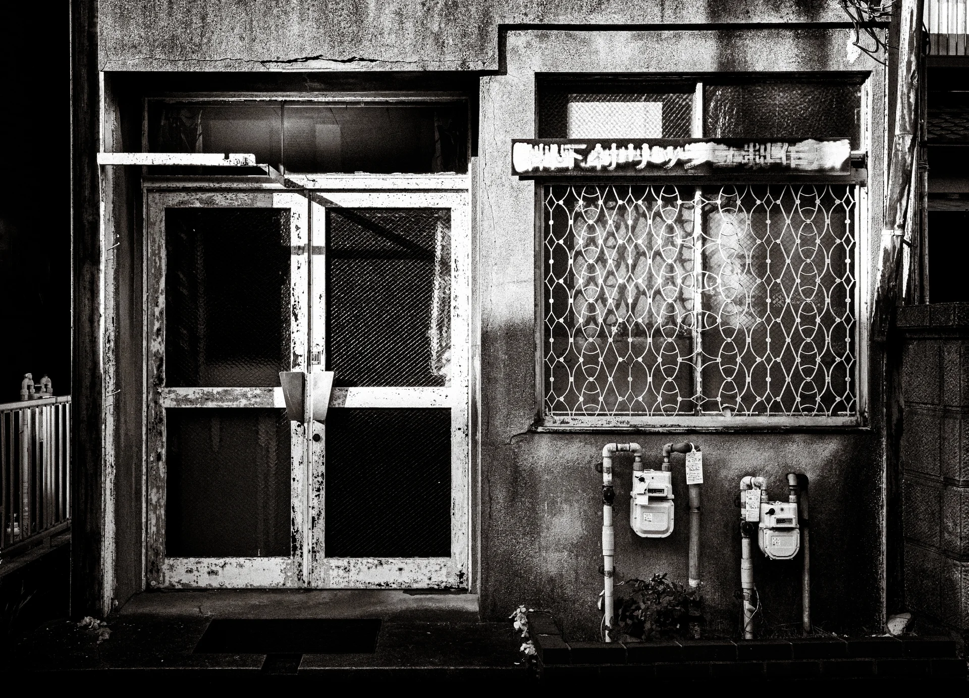 A worn mesh-paneled door stands beside a diamond-grilled window and two utility meters in black and white.
