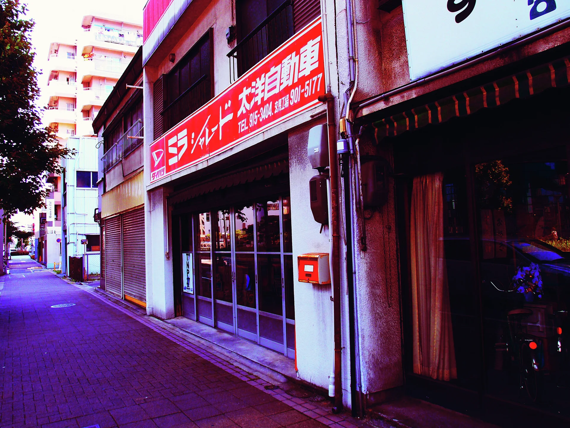 A long red sign tops glass doors along a narrow lane lined with weathered buildings.