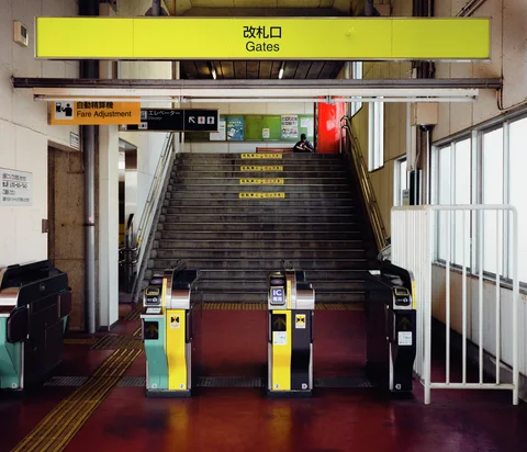 Yellow ticket gates stand before a broad staircase beneath a yellow overhead sign.