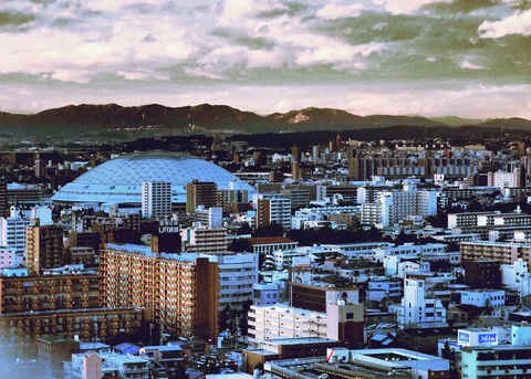 A large pale domed roof rises among city buildings with dark mountains stretching across the background.