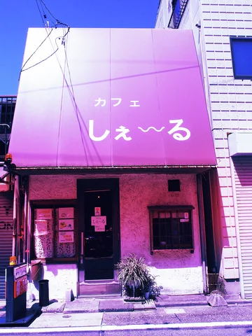 A broad pink cafe sign hangs above a small dark doorway and potted plant.
