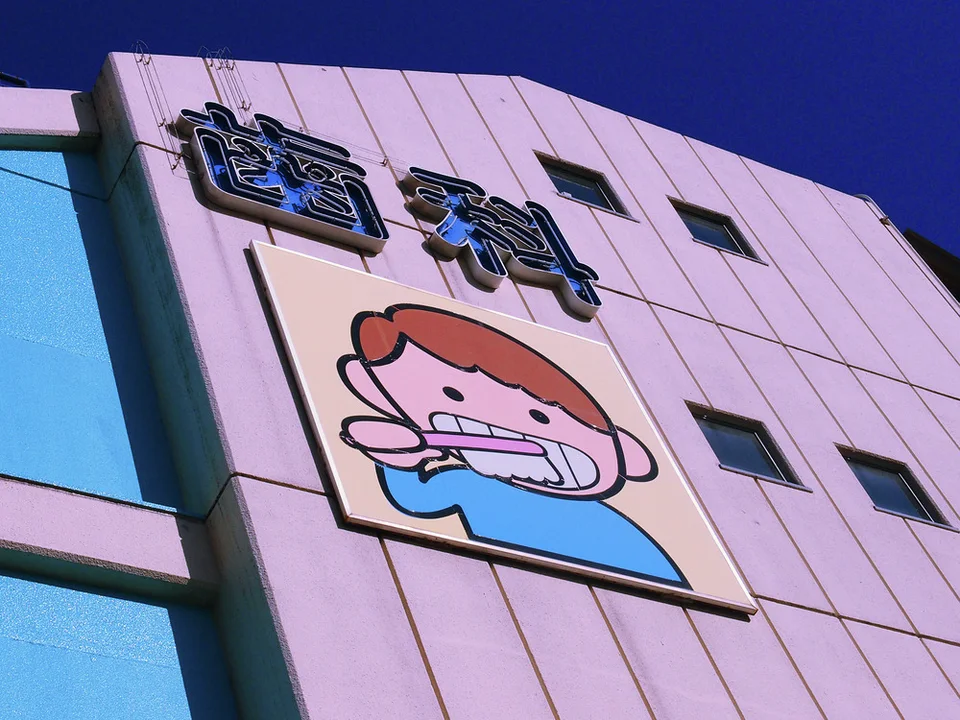 A cartoon child brushing teeth decorates a pale pink building beneath raised Japanese dental lettering.