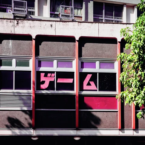 Bold pink lettering fills dark windows beneath weathered concrete balconies beside leafy greenery.