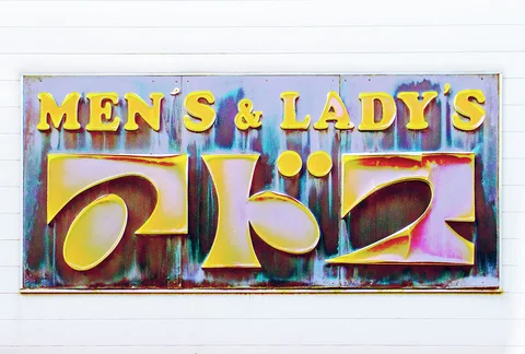 Gold Men's and Lady's lettering sits above large raised Japanese characters on a weathered reflective sign.