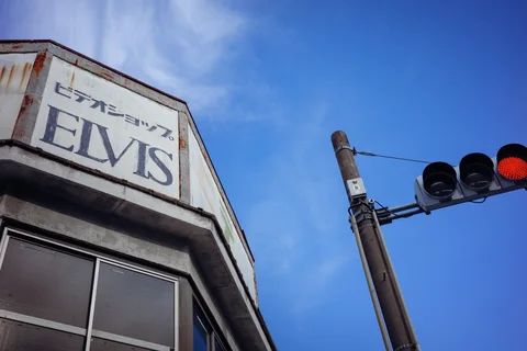 An ELVIS sign and red traffic light rise against a bright blue sky.