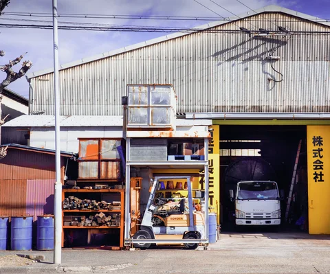 A small white truck occupies an open workshop bay beside shelving and a forklift.