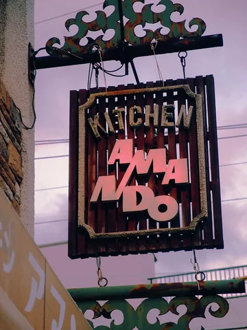 A framed hanging Kitchen sign displays irregular pink letters beneath decorative curled metal brackets.