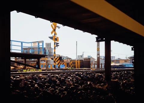 Railway tracks and crossing equipment appear through a shadowed structure above gravel ballast.