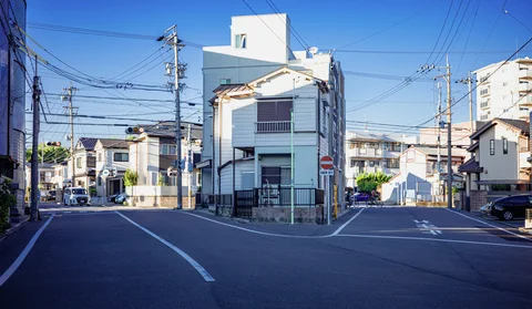 Two quiet streets diverge around a narrow white building beneath a dense network of overhead wires.