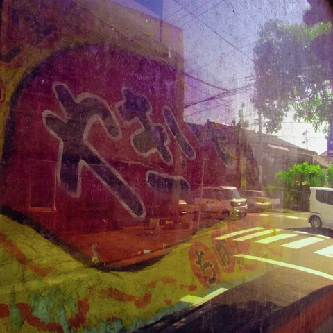 A faded red circular shop graphic overlaps window reflections of cars, trees and a pedestrian crossing.
