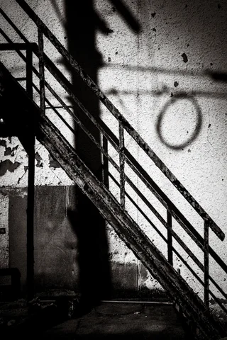 A diagonal metal stair railing casts angular shadows across a wall marked with a circle in black and white.