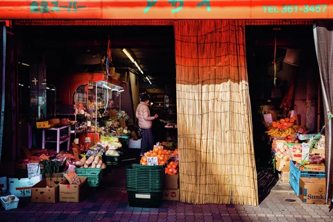 A produce shop displays fruit and vegetables around a large bamboo blind, with a person standing inside.