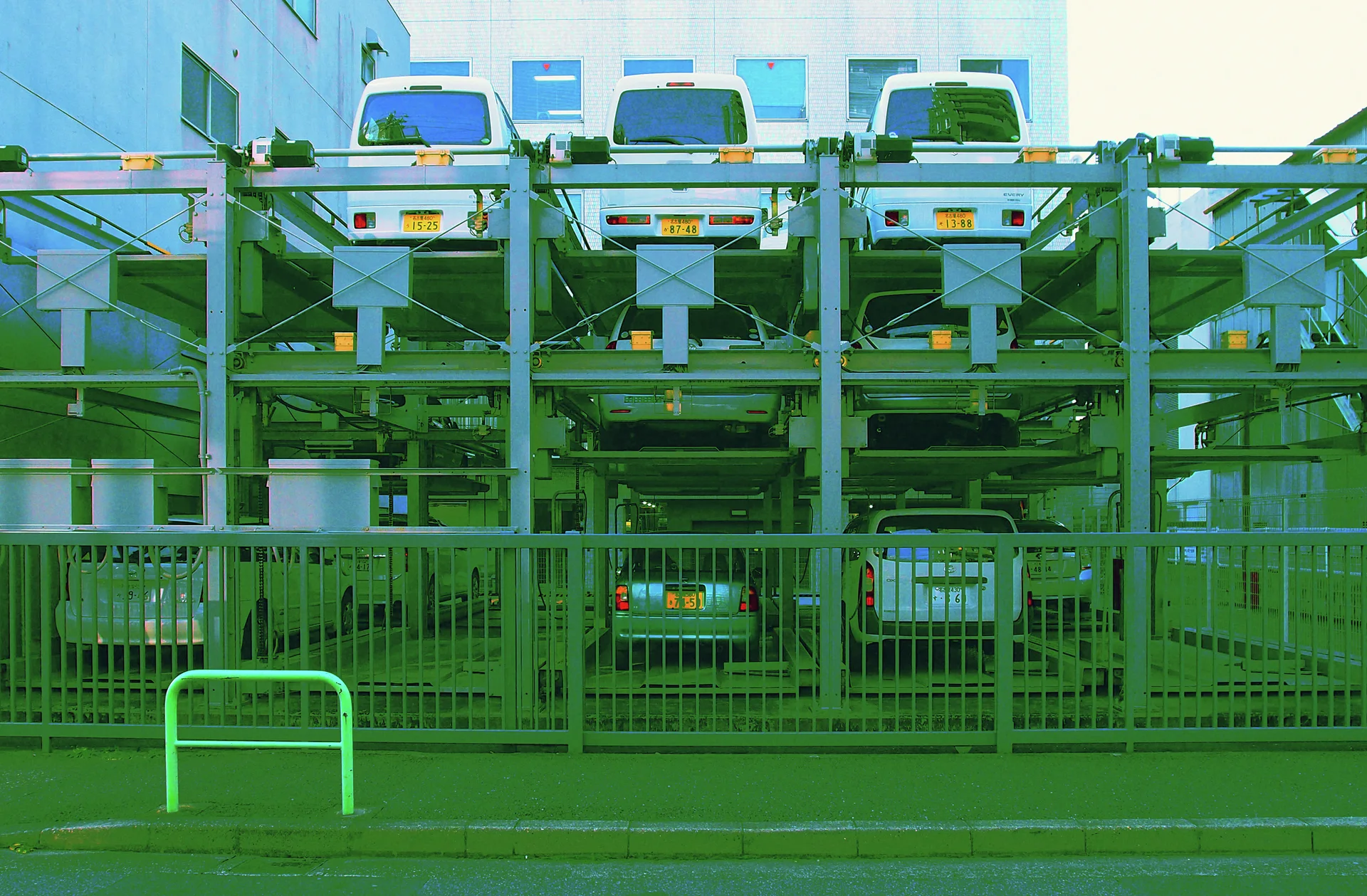 White vans occupy the upper level of a steel parking rack behind a fence.
