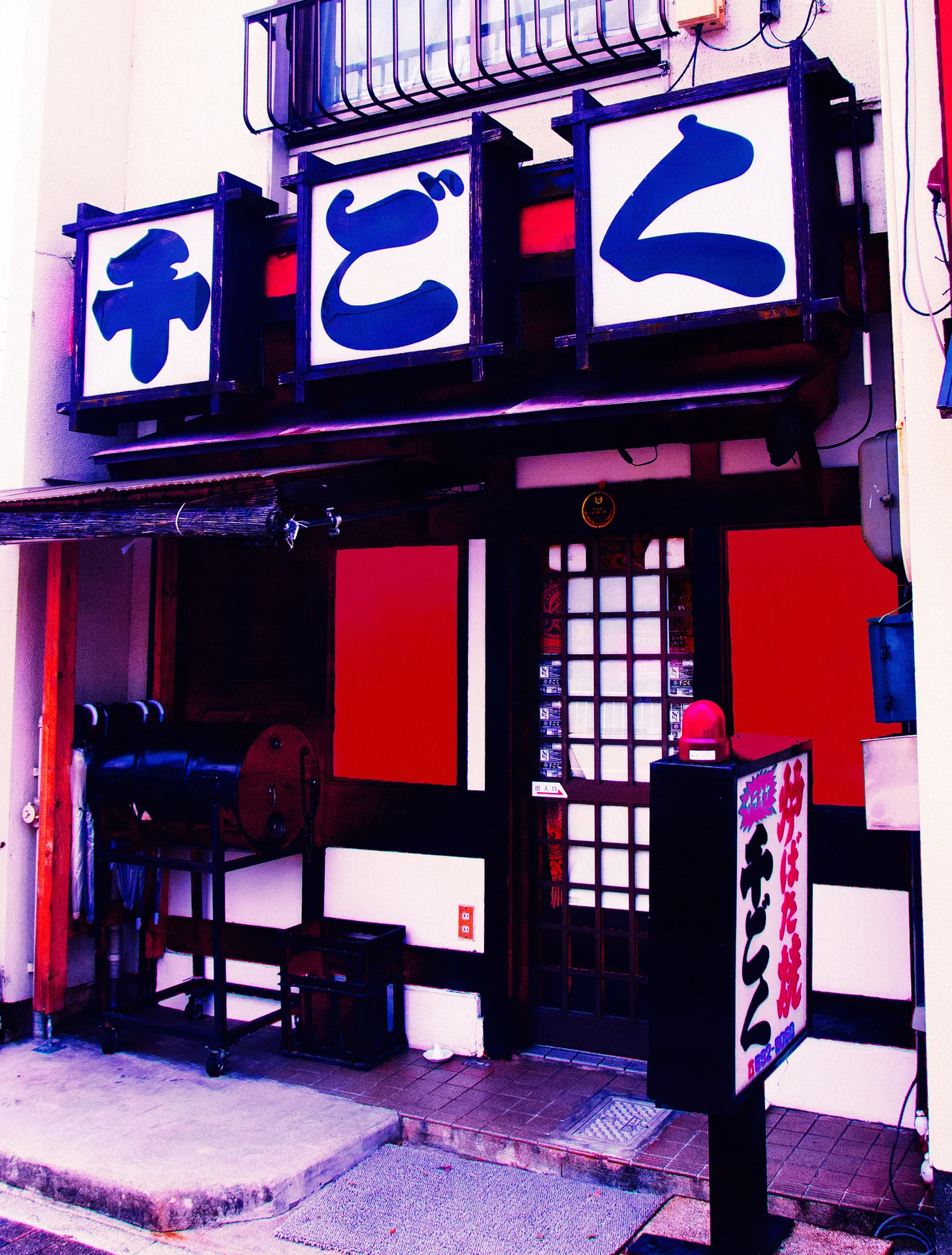 Large blue characters hang above a black, white, and red storefront with a gridded door.