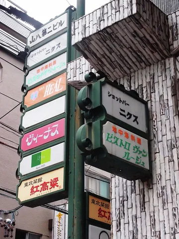 A tall stack of narrow colored business signs rises beside a pale vertically textured building facade.